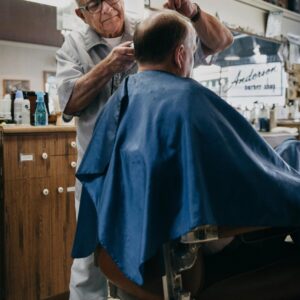 An elderly barber skillfully cuts a client's hair in a traditional barbershop setting.