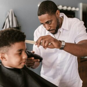 Barber in a white shirt carefully trimming a boy's hair at a salon.